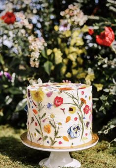 a decorated cake sitting on top of a white plate in front of some bushes and flowers