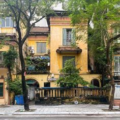 an old yellow building with many windows and balconies on the second floor is surrounded by trees