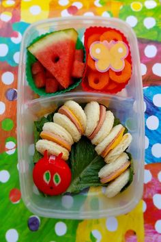 a plastic container filled with fruit and veggies on top of a colorful table cloth