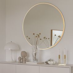 a white dresser topped with a round mirror and vase filled with flowers on top of it