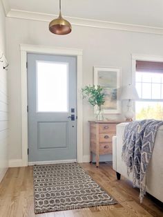 a bedroom with white walls and wood floors has a blue door, rugs, and lamp