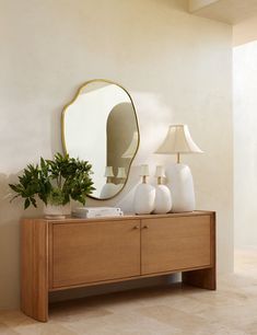 a wooden dresser topped with white vases and a large mirror on top of it