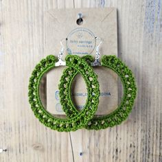 pair of green crocheted hoop earrings hanging on wooden wall next to package with tag