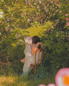 a woman sitting on top of a wooden chair in front of a lush green field