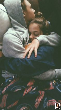 two people laying on a couch with their arms around each other and one person kissing the other