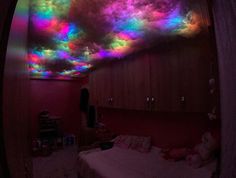 a room with a bed and colorful lights on the ceiling above it is a rainbow - colored cloud