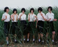 a group of young women standing next to each other in front of tall green grass