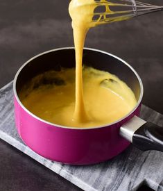 a whisk is being poured into a pan filled with yellow sauce on a gray surface