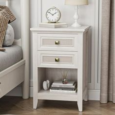 a white night stand with two drawers and a clock on the top shelf next to it