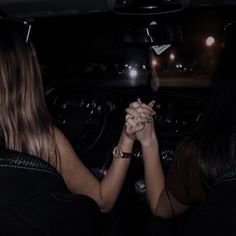 two women are holding hands in the back of a car at night with lights on