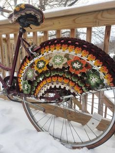 an old bicycle is decorated with crochet and flowers in the snow on a deck