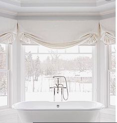 a white bath tub sitting under a window next to two windows with drapes on them