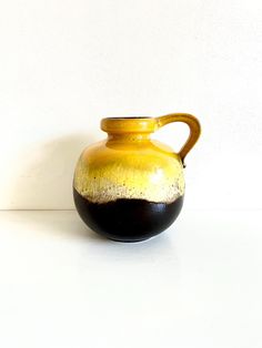 a yellow and black vase sitting on top of a white table next to a wall