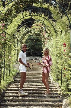 a man and woman holding tennis racquets on top of a set of stairs