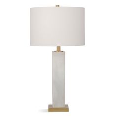 a white table lamp with a gold base and a light shade on it's side