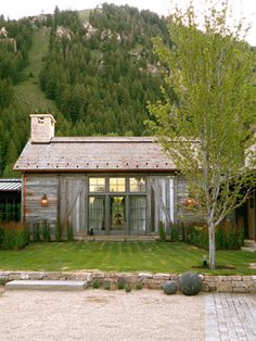 a small house with a tree in the front yard and mountains in the back ground