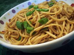 a white bowl filled with noodles and green onions on top of a polka dot tablecloth