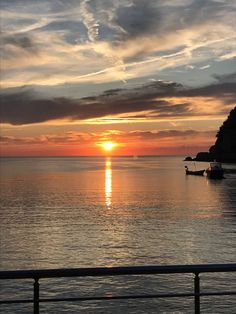 the sun is setting over the ocean with boats in the water