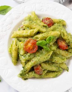 a white plate topped with pasta covered in pesto sauce and tomatoes on top of it