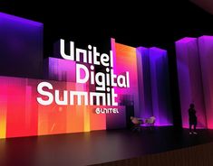 a man standing in front of a large screen with the words united digital summit on it