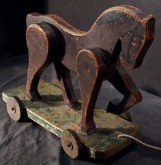 an old wooden toy horse on a black sheeted surface with a cord attached to it