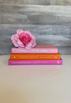 three books stacked on top of each other with a pink flower in the middle one