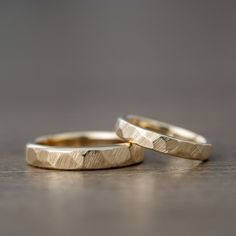 two gold wedding rings sitting on top of a wooden table