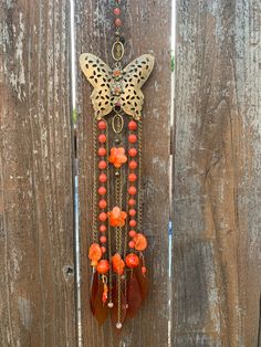 a butterfly hanging on a wooden fence with orange beads and other items attached to it