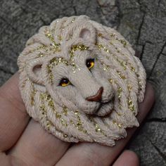 a hand holding a white lion brooch with gold sequins