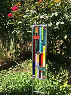 a colorful stained glass window sitting on top of a metal stand in front of some flowers