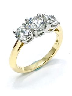 three stone diamond ring in yellow gold with diamonds on the sides and shoulders, set against a white background