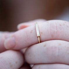 a close up of a person's hand holding a gold ring with a bar on it