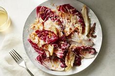 a white plate topped with red cabbage next to a fork and glass of wine on top of a table