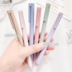 a person holding five different colored pens in their hand