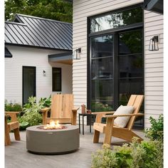 a fire pit sitting on top of a patio next to wooden chairs and tables in front of a white house