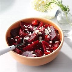 a bowl filled with beets and feta cheese next to a vase full of flowers