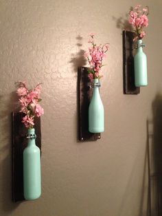 three blue vases with pink flowers in them are hanging on the wall next to each other