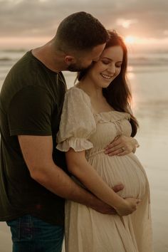 a man and woman standing next to each other on the beach with their pregnant belly