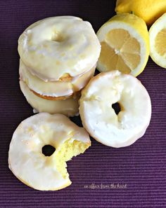 lemon donuts with white frosting and sliced lemons on a purple mat next to them