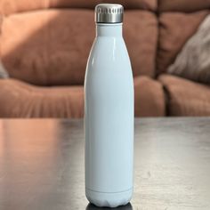 a white water bottle sitting on top of a wooden table next to a brown couch