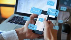 a person holding a cell phone in front of a laptop with blue envelopes on it