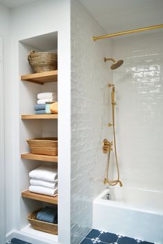 a bathroom with white walls and blue floor tiles on the shower wall, shelving in the bathtub