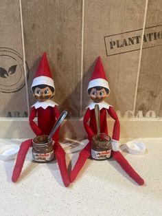 two elfs sitting next to each other on top of a counter with jars and spoons in front of them