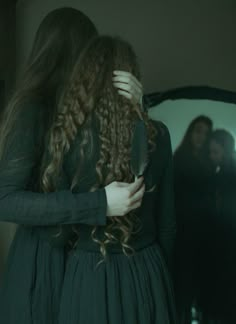 a woman with long curly hair standing in front of a mirror and holding her head