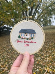 someone is holding up a small embroidered ornament in front of some trees and leaves