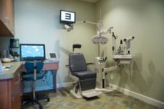 a dentist chair sitting in the corner of a room next to a desk and monitor