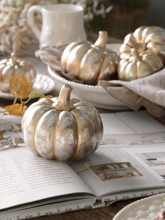 a table topped with lots of white pumpkins on top of a wooden table next to plates