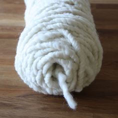 a roll of white yarn sitting on top of a wooden floor