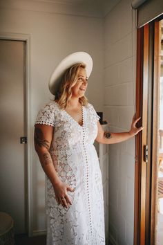 a woman wearing a white dress and hat standing in front of a door with her hand on the glass