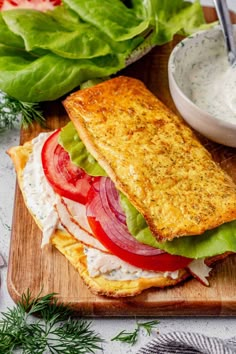 a sandwich with tomatoes, lettuce and tomato slices on a wooden cutting board